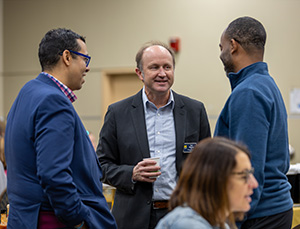 Three people engaged in conversation, one holding a cup, in a casual setting.