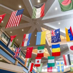 A display of various international flags hanging from the ceiling of an academic building's three-story atrium.