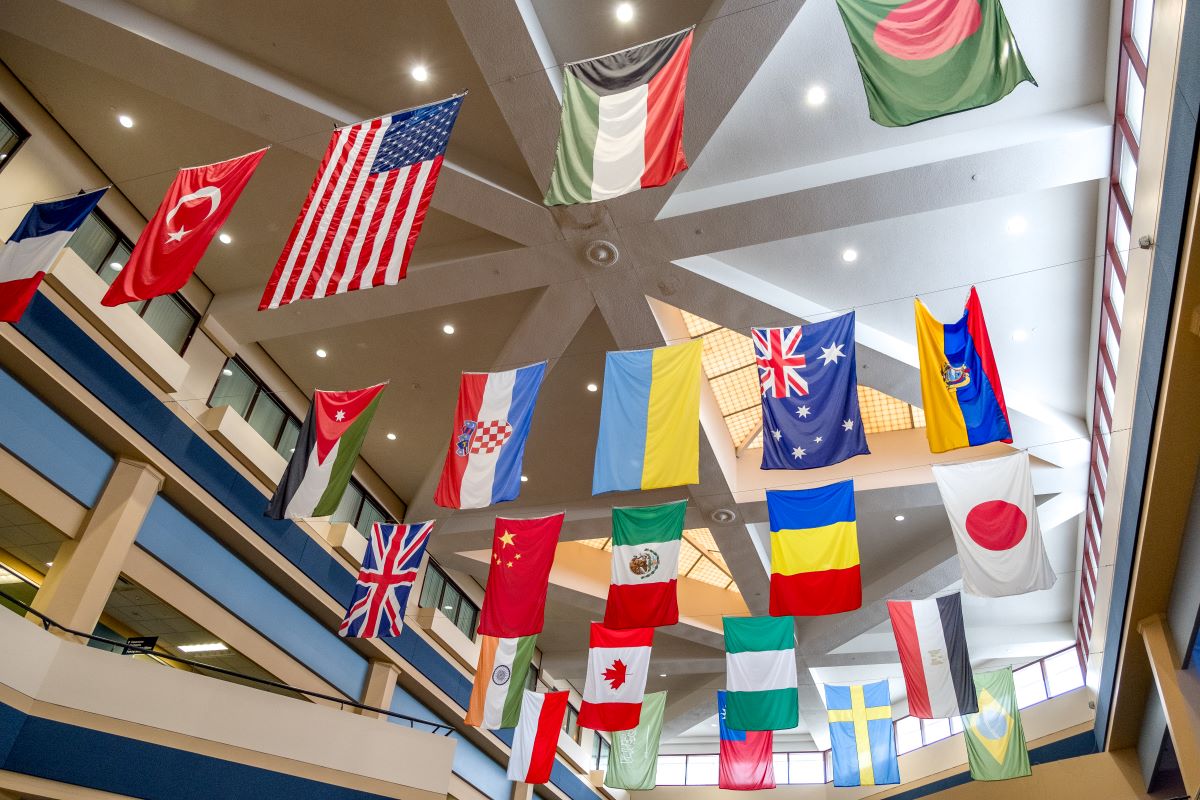A display of various international flags hanging from the ceiling of an academic building's three-story atrium.
