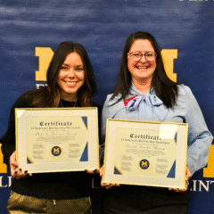 Two women holding certificates of Employer Partnership Excellence in front of a blue backdrop with "M FLINT" logo.