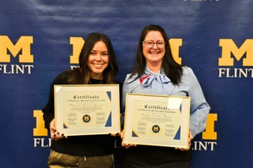 Two women holding certificates of Employer Partnership Excellence in front of a blue backdrop with "M FLINT" logo.