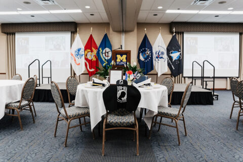 A round table set for an event, featuring military flags, a POW-MIA chair cover, and decorative flowers.