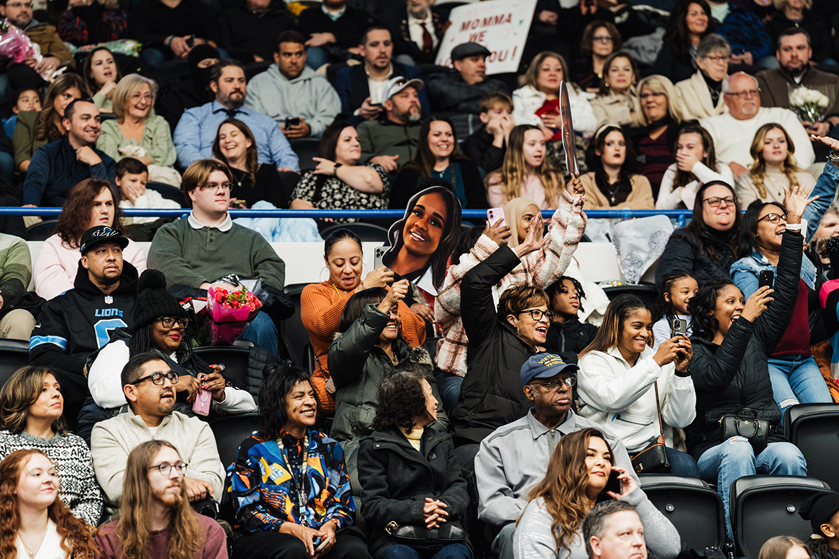 A crowded audience at an event, with many people holding phones and some displaying signs.