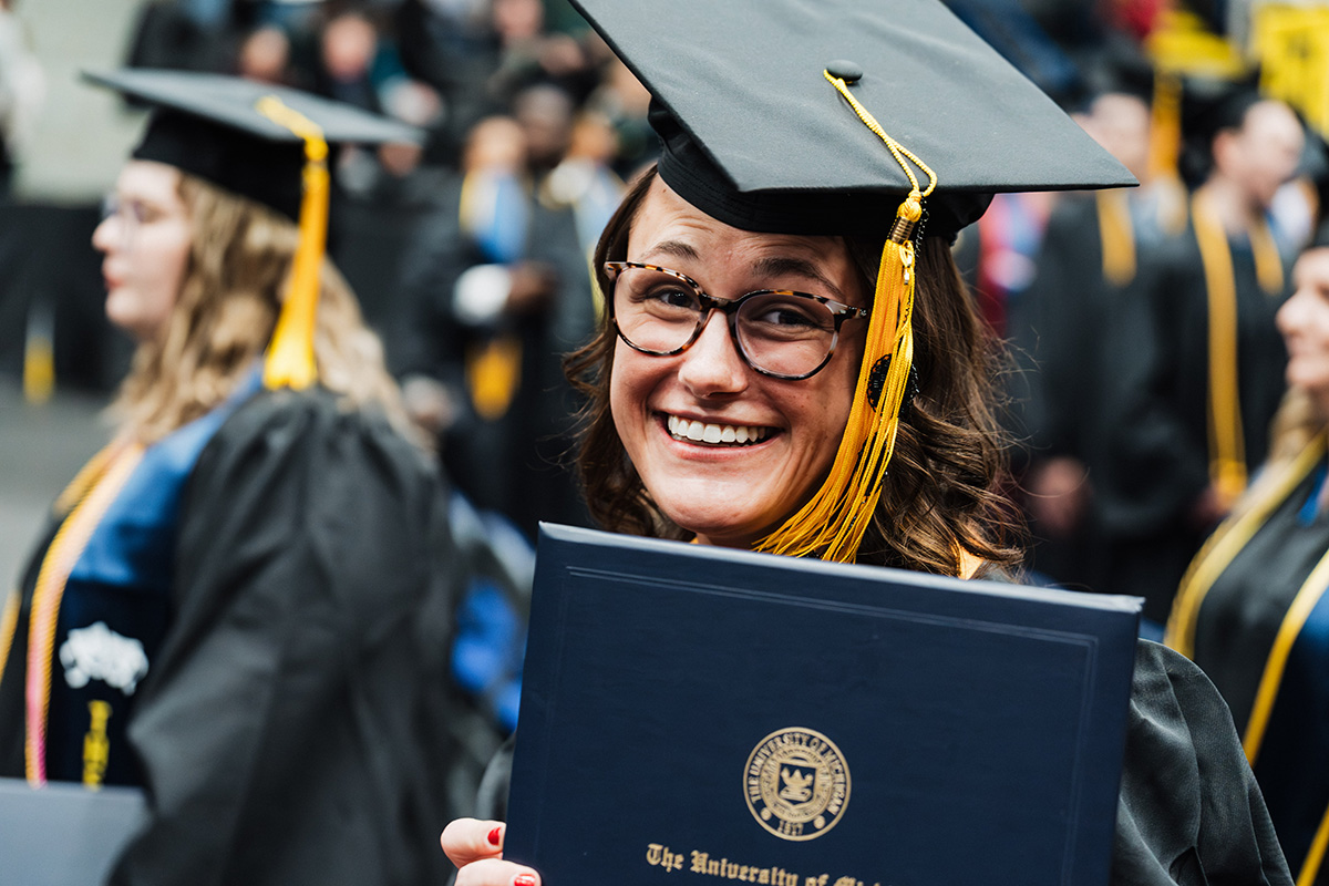A graduate in a black cap and gown holds a diploma from the University of California during a graduation ceremony.