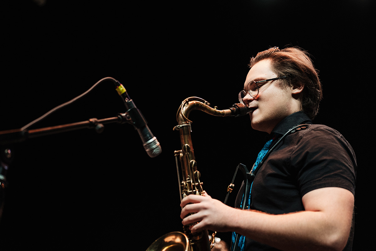A musician playing a saxophone on stage, with a microphone positioned nearby.