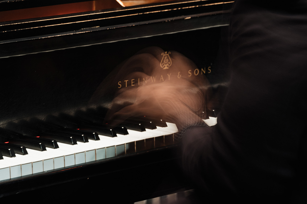 A blurred hand playing a piano with the brand name "Steinway & Sons" visible on the piano's surface.