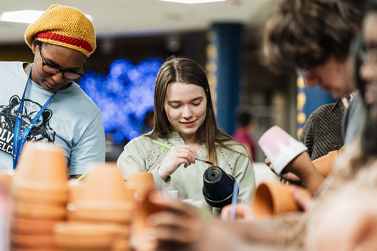 A group of people engaged in a pottery painting activity, with various clay pots and painting tools on the table.