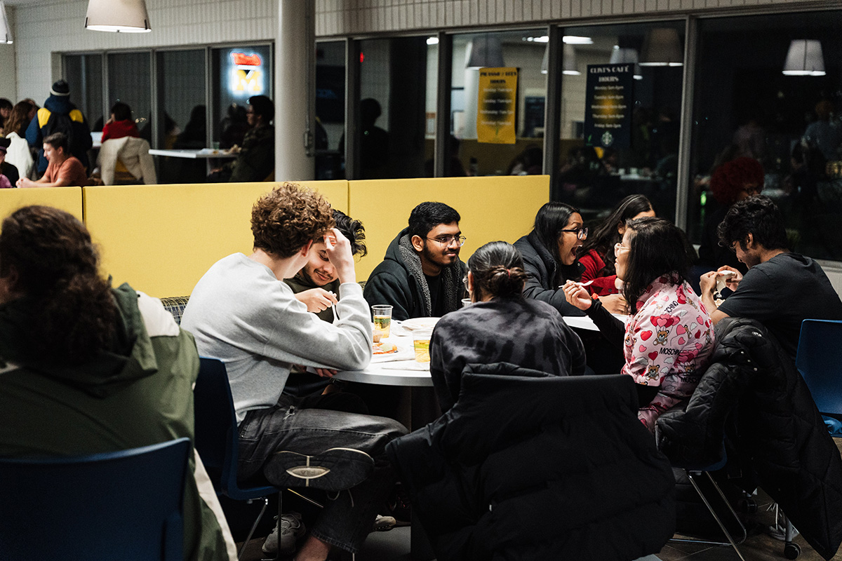 A group of people sitting around a table in a dining area, engaged in conversation and eating.