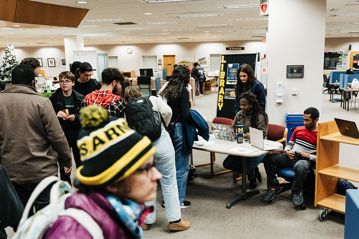 A group of people gathered around a table in a library, with a sign that reads "LIBRARY" in the background.