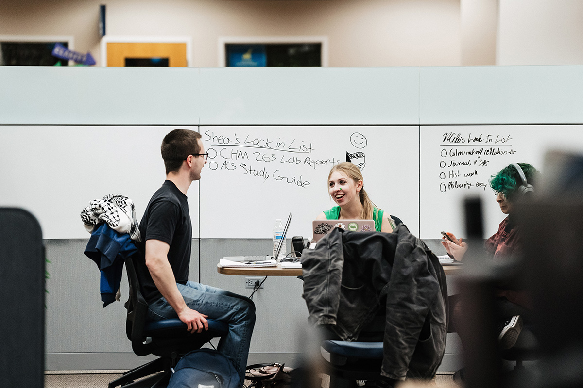 A study group at a table with whiteboards listing tasks: "Shea's Lock in List," "CHM 263 LOB Reports," and "AS Study Guide."