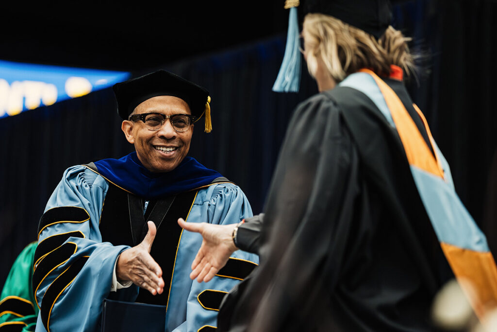 Laurence Alexander smiling and shaking hands with a graduating student. 