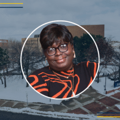 A circular portrait of a person wearing a black and orange striped sweater, with a snowy campus background.