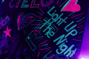 Colorful neon chalk writing on a dark background reads "Light Up the Night," surrounded by hearts and stars.