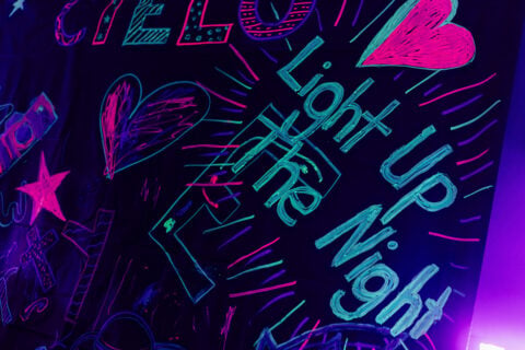 Colorful neon chalk writing on a dark background reads "Light Up the Night," surrounded by hearts and stars.