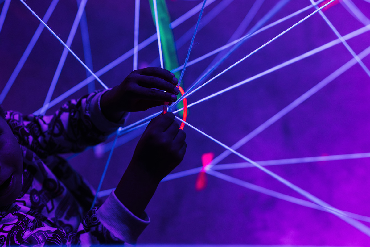 FLINT_Light Up the Night 2026_0018 A child's hands are manipulating colorful strings in a dark space illuminated by purple light.