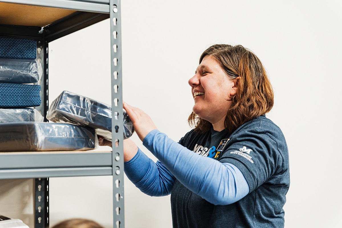 A person is reaching for a package on a shelf, surrounded by neatly stacked items in a storage area.