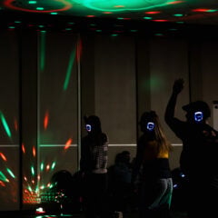 A group of people dancing in a dimly lit room with colorful lights and wearing wireless headphones.