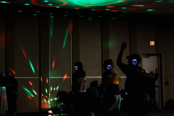 A group of people dancing in a dimly lit room with colorful lights and wearing wireless headphones.