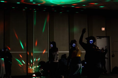 A group of people dancing in a dimly lit room with colorful lights and wearing wireless headphones.