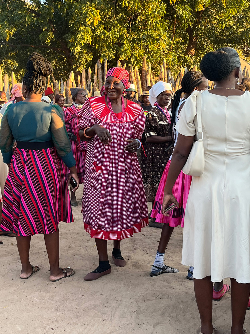 A group of women in colorful traditional attire gathered outdoors, with some wearing bright pink dresses and others in various styles.