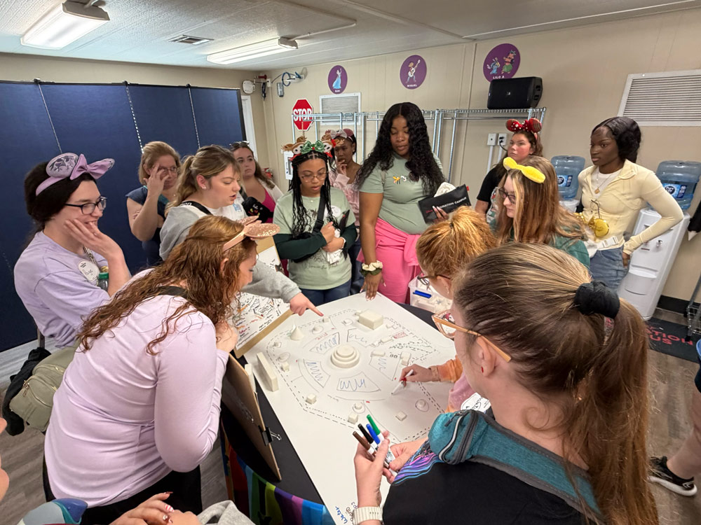 A group of people gathered around a table, engaging in a creative activity involving drawing and writing on a large paper.