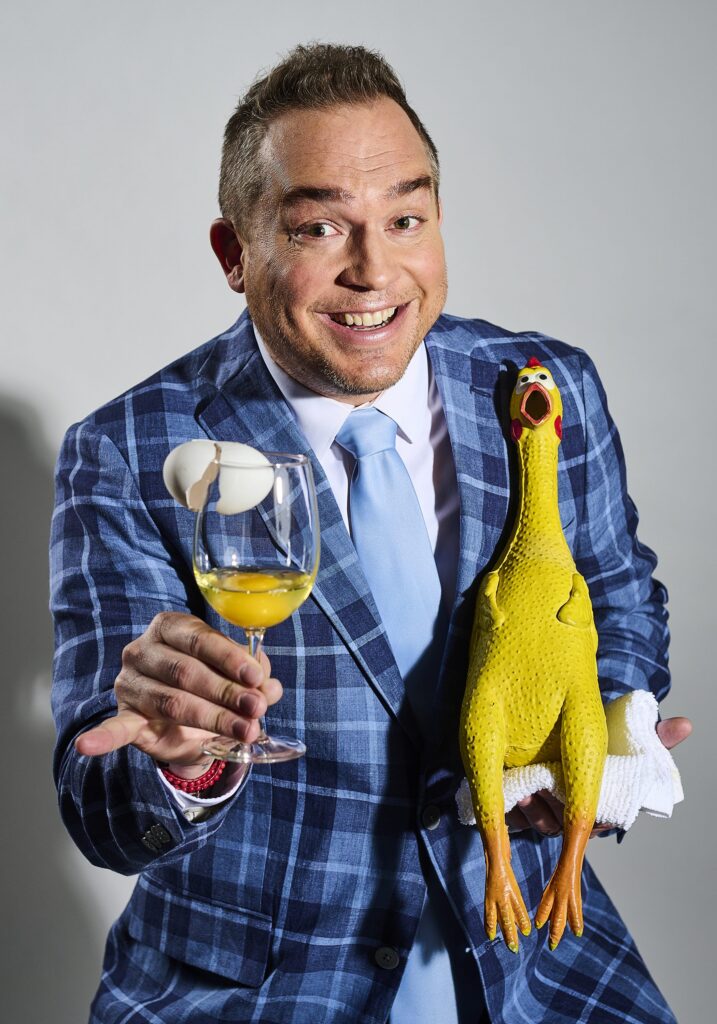 Michael Kent wearing a blue plaid suit holding a rubber chicken