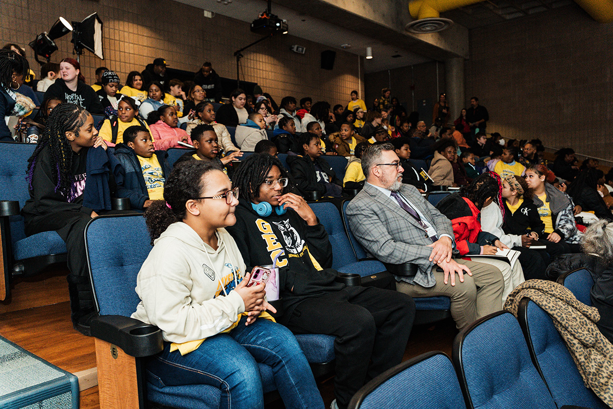 FLINT_Revving Up STEM 2026_0005 A group of children and adults seated in an auditorium, some wearing matching yellow shirts, engaged in an event.