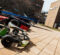 A go-kart and two race cars are parked on a paved area in front of a university building, with trees in the background.