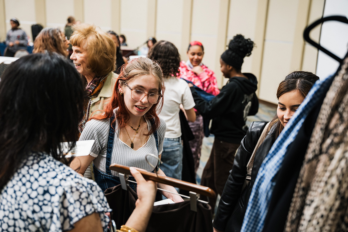 A group of people is gathered at a clothing exchange event, with individuals holding garments and interacting with each other.