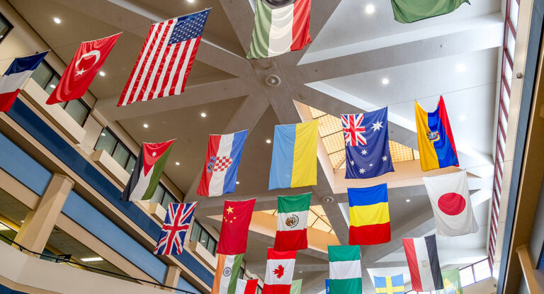 A variety of international flags hanging from the ceiling in a spacious indoor area, showcasing cultural diversity.