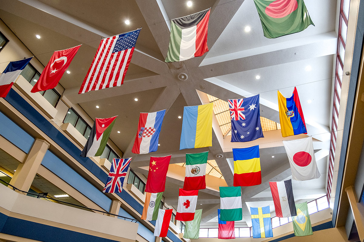A variety of international flags hanging from the ceiling in a spacious indoor area, showcasing cultural diversity.