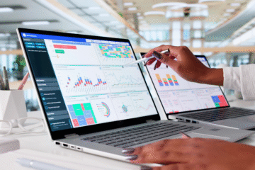 A person is using a stylus to interact with data visualizations on two laptops displaying a KPI dashboard, with various charts and graphs.