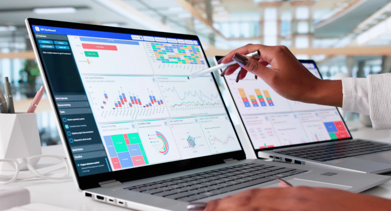 A person is using a stylus to interact with data visualizations on two laptops displaying a KPI dashboard, with various charts and graphs.