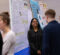A group of people is engaged in discussion at a science fair, with several research posters displayed in the background.