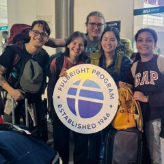 A group of travelers at an airport holding a sign for the Fulbright Program, surrounded by luggage and backpacks.