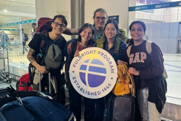 A group of travelers at an airport holding a sign for the Fulbright Program, surrounded by luggage and backpacks.