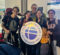 A group of travelers at an airport holding a sign for the Fulbright Program, surrounded by luggage and backpacks.