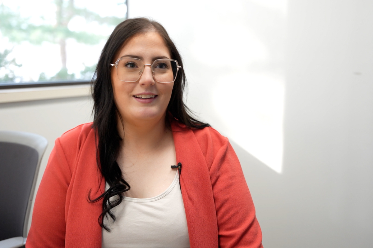 A person wearing a red blazer and a light-colored top is seated in front of a window with natural light.