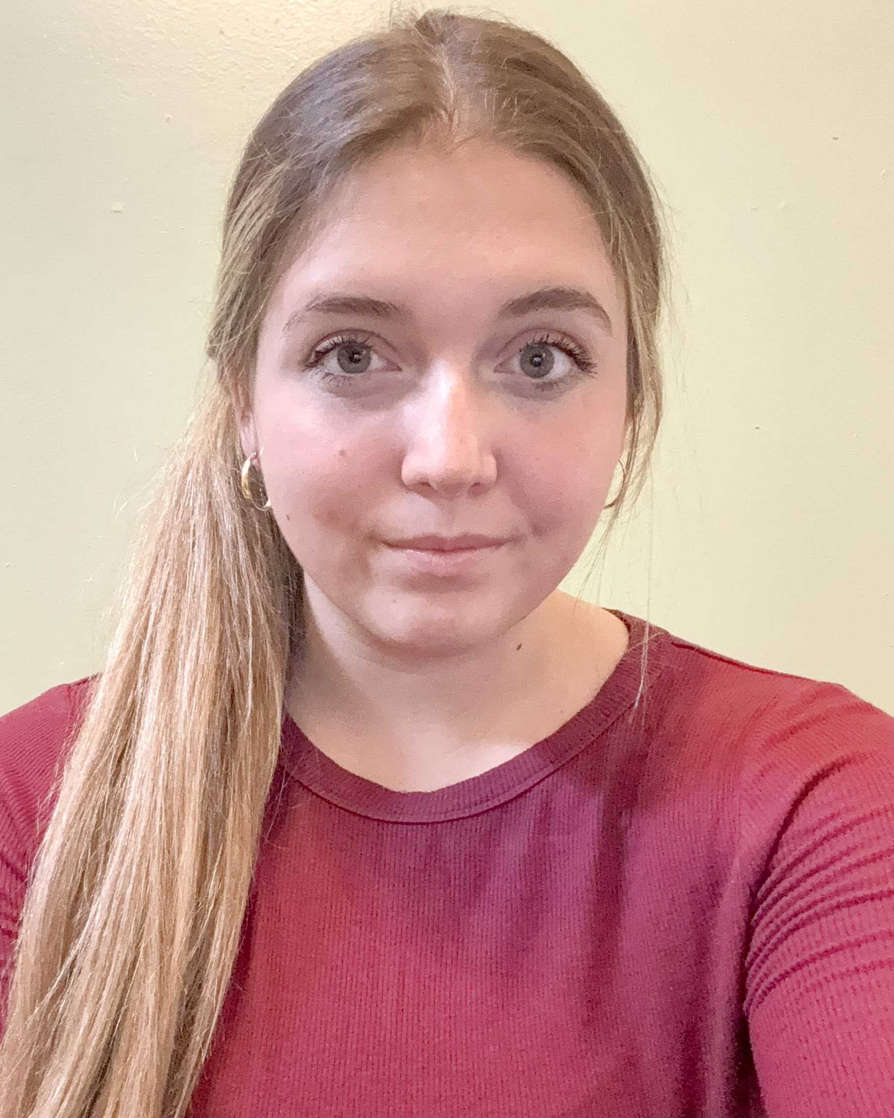 A young woman with long, blondish-brown hair poses for a self-portrait. She is wearing a dark-red, long-sleeved shirt.