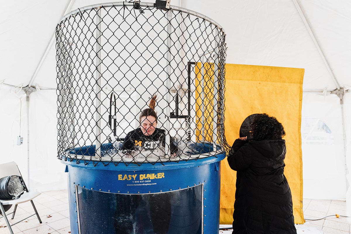 Person inside a dunk tank with water splashing, another person standing outside watching.