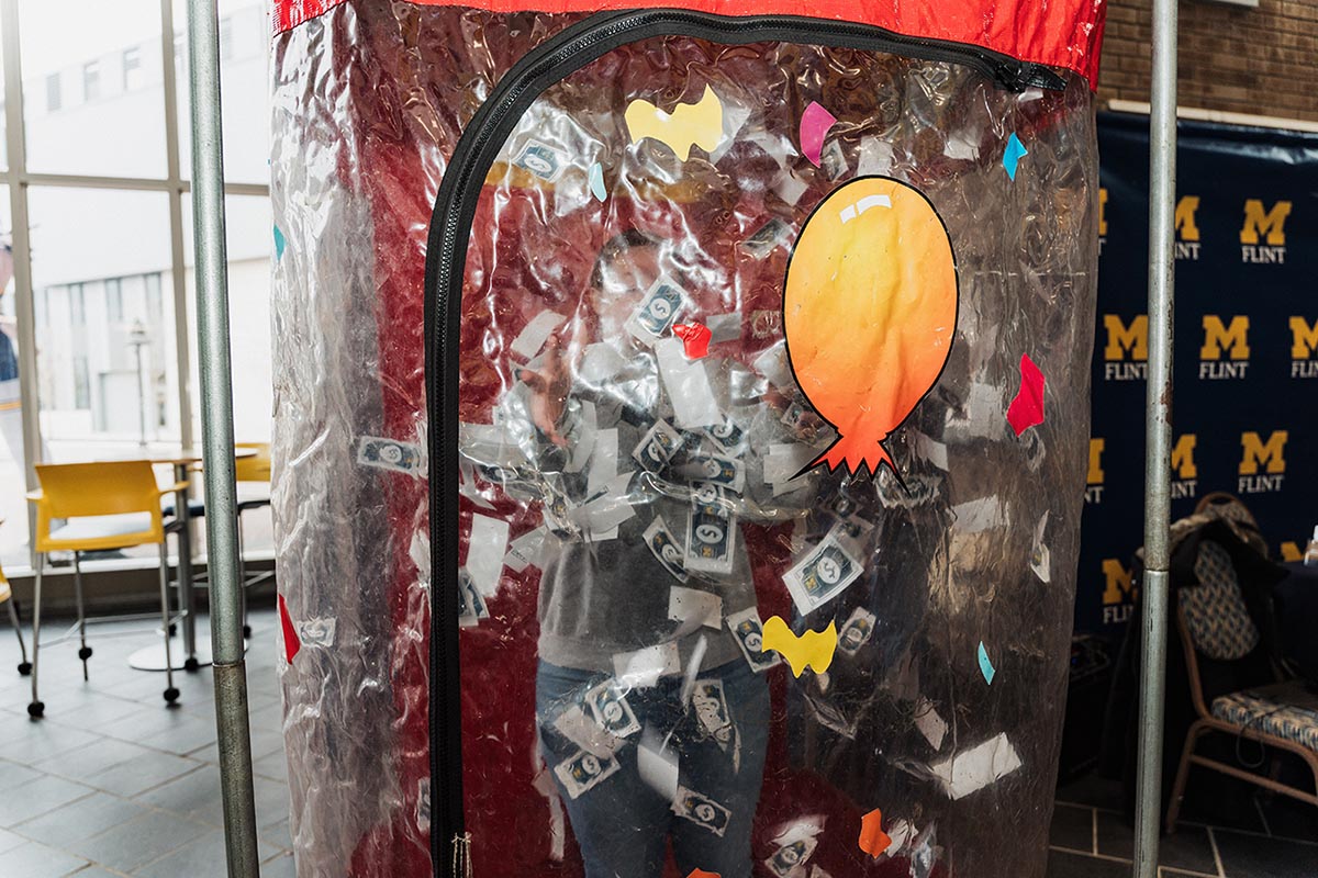 Person inside a transparent inflatable money booth with fake dollar bills swirling around.