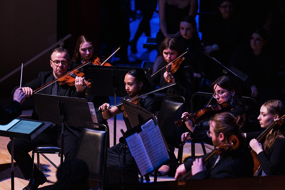 Orchestra string section performing on stage with musicians playing violins and violas.