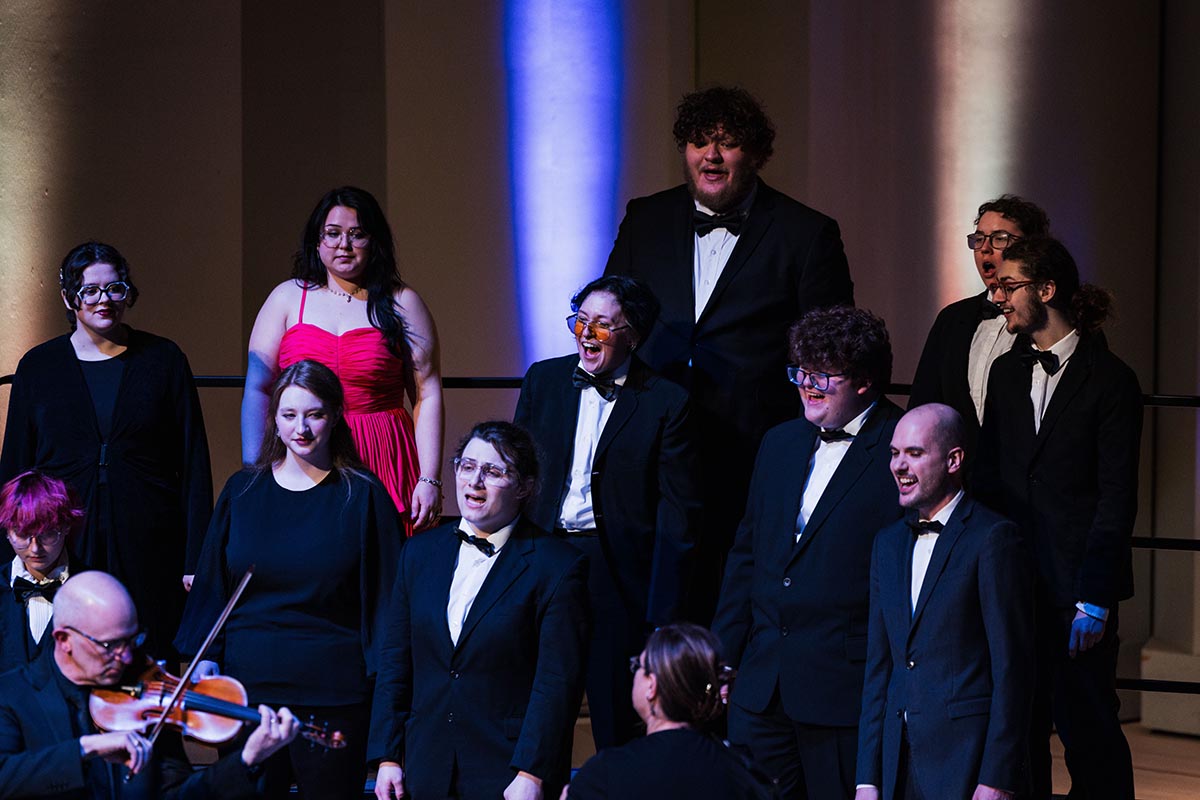 Group of formally dressed people performing on stage, with one person playing violin.