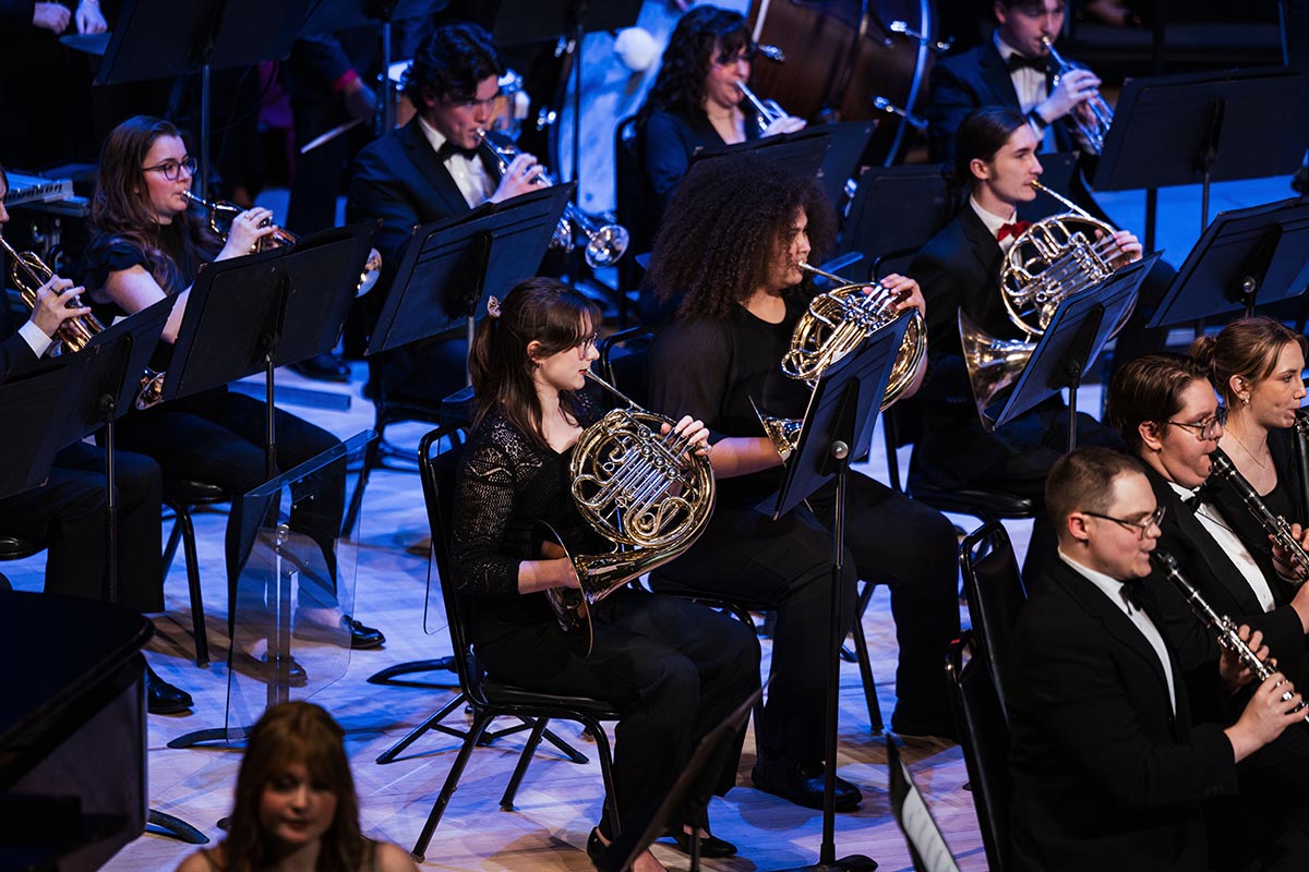 Orchestra musicians playing brass and woodwind instruments during a performance.
