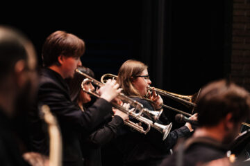 A group of musicians playing brass instruments, including trumpets and a trombone, on stage in a dark setting.