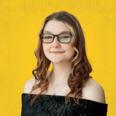 Person with long curly hair wearing an off-shoulder black top against a yellow background.