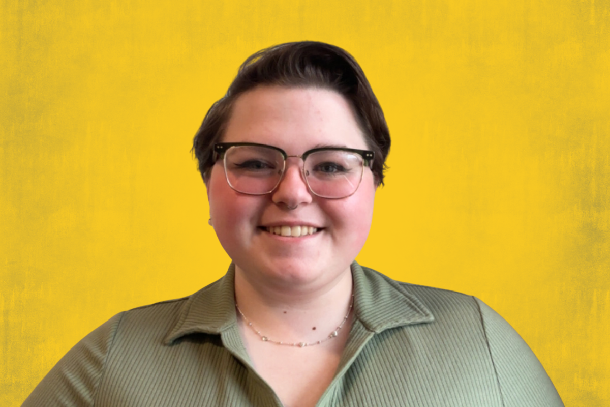 Person wearing a green ribbed shirt and a delicate necklace against a yellow background.