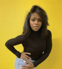 Person wearing a black long-sleeve top and light blue jeans posing against a yellow background.