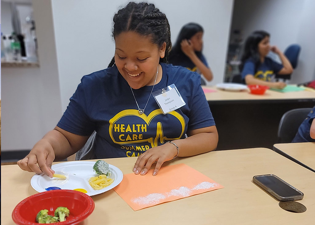 A health care summer camp attendee using food to create arts & crafts.