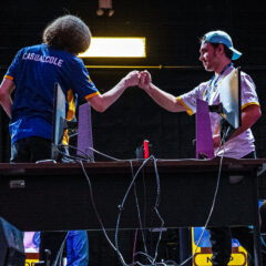 Two esports players fist bump over a desk with gaming monitors during a competition.
